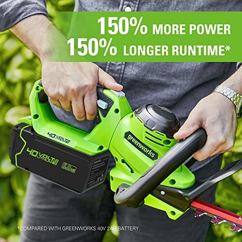 Person using a green Greenworks hedge trimmer with a battery.