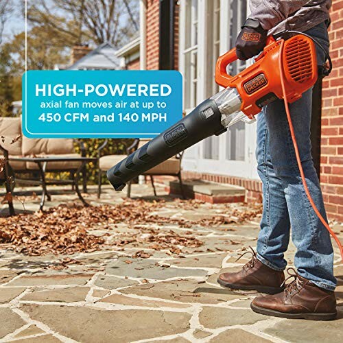 Person using an orange leaf blower on a stone patio near a house.