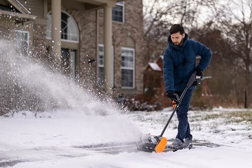 Man using snow blower on driveway in winter.